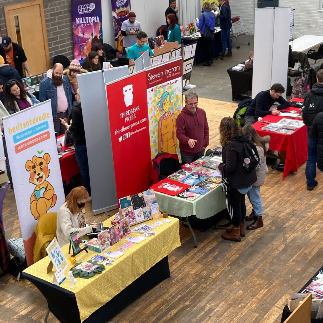 Photo of the Drillhall from above, with tables laden with comics and small press books. Photo of the Drillhall from above, with tables laden with comics and small press books.