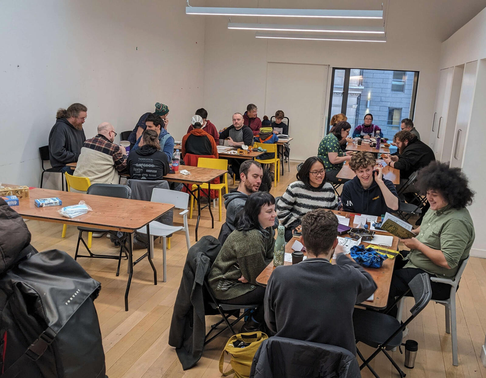 Photo from the board game zone at TAGS 23; long tables have seats around them with many people playing and smiling. Only a few guests are wearing masks.